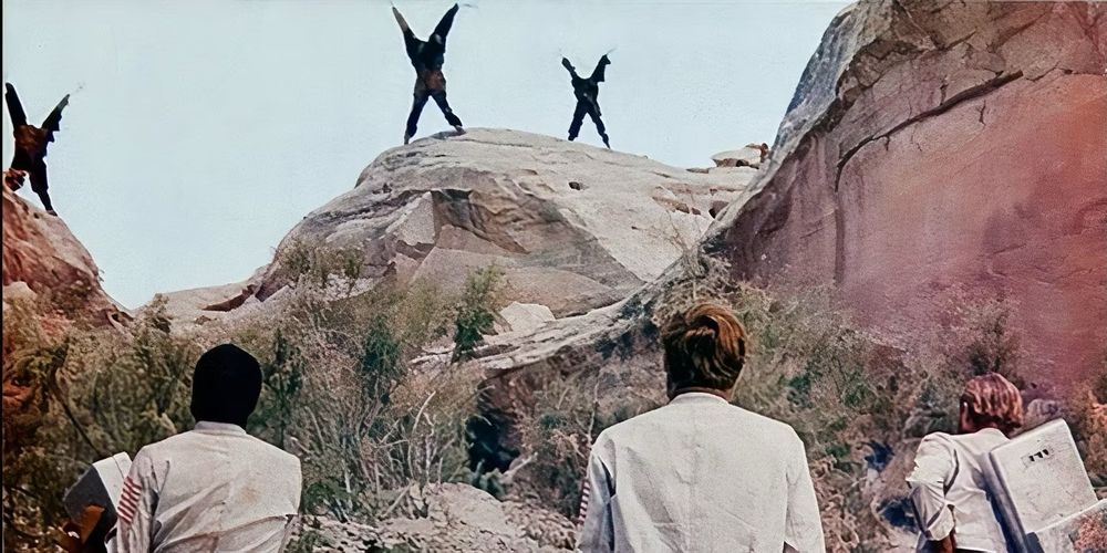 Screenshot from the film, “Planet of the Apes” (1968) showing human astronauts looking up at a clifftop, marking the edge of The Forbidden Zone, where the flayed hides of apes are displayed on x-shaped crosses, as a warning not to enter.