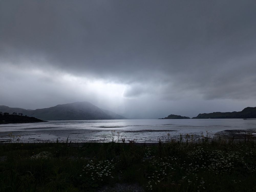 Dark skies above, rain over the water and the sun trying to force through  it's a colour photo, but looks black and white as the weather takes a turn for the worse.