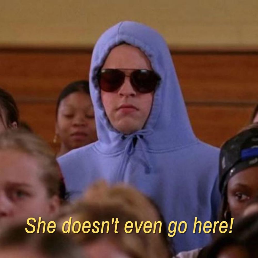 Image of Damian from "Mean Girls" wearing a hoodie and sunglasses in the gym crowd scene with the dialogue text at the bottom: "She doesn't even go here!"