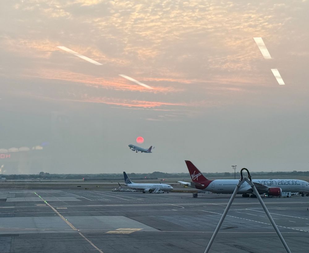 Airplane taking off with the rising sun behind it and parked planes in the foreground 