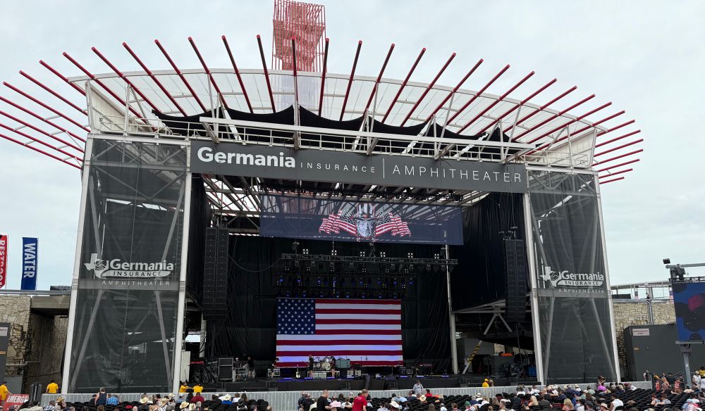 Stage at amphitheater with large American flag hung in back and drawing above of Willie Nelson 