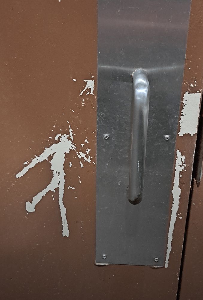 The door's paint stripes forme the silhouette of a person running. And the handle looks like a face.
