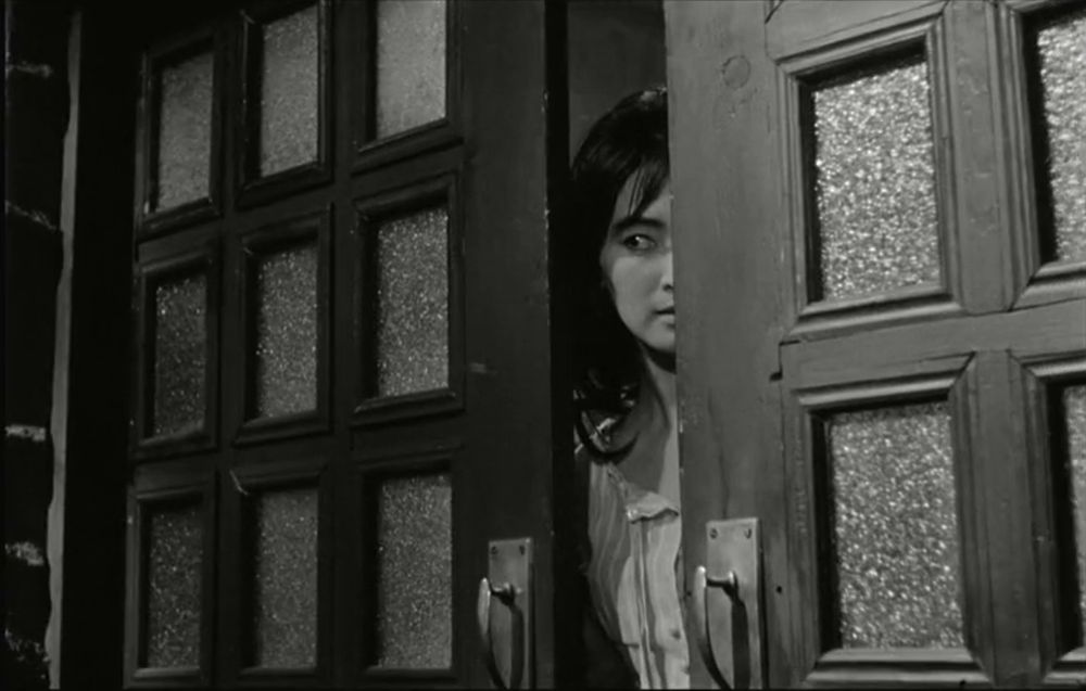 Black and white frame from the South Korean psychological thriller '하녀'(Hanyeo)/'The Housemaid' (1960). Young Korean woman (Lee Eun-shim as Myung-sook) peeking through the slightly opened sliding doors.