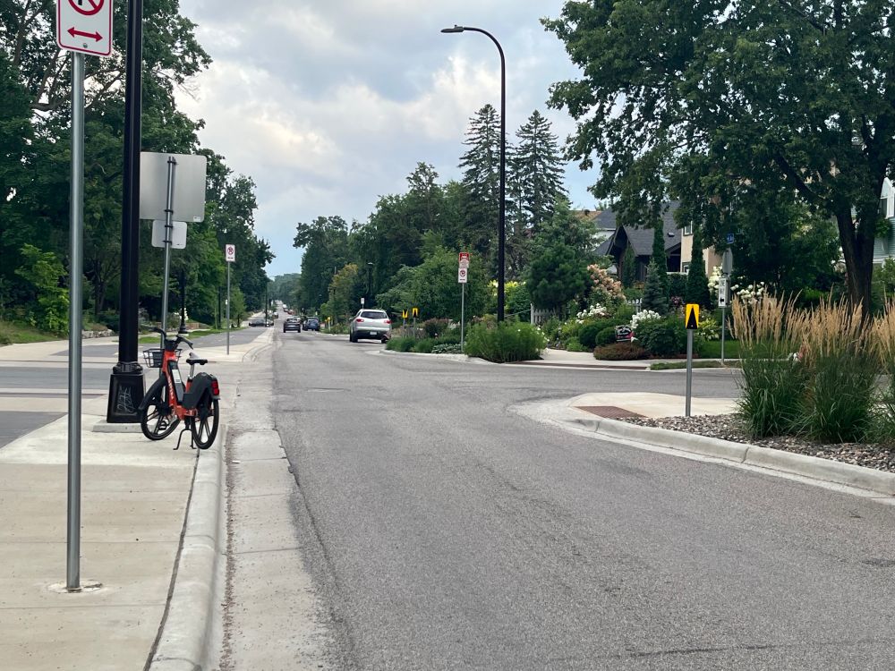 Image of a narrow crossing on a one-way street with an orange rental bike, parked on the curb on the left-hand side of the street
