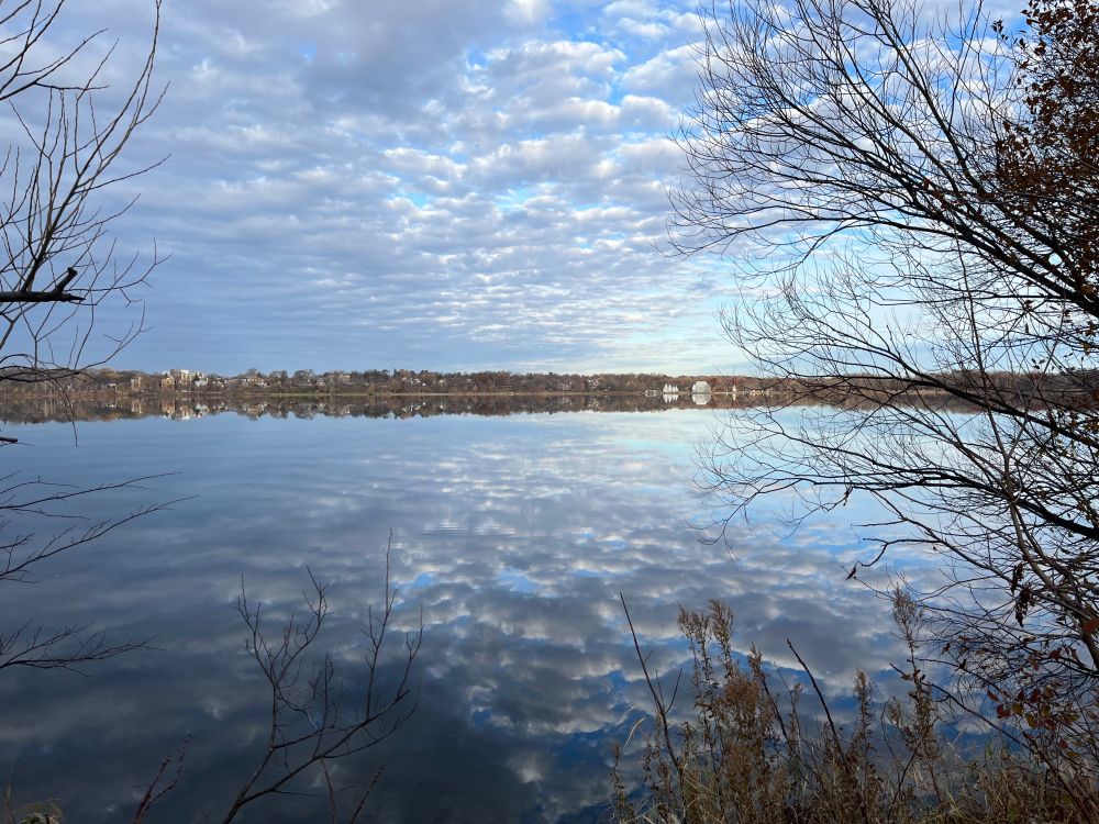 Image of calm lake reflecting blue skies with white clouds. 