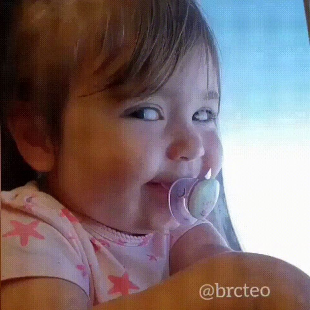 a little girl with a pacifier in her mouth is smiling