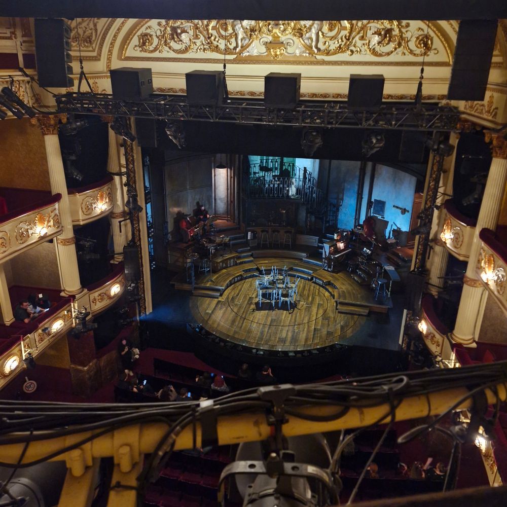 Picture of the stage at the Lyric Theatre from quite high up. The stage is set for Hadestown, with musical instruments at the side, a balcony at the back, and chairs stacked on tables in the middle of the turntable 