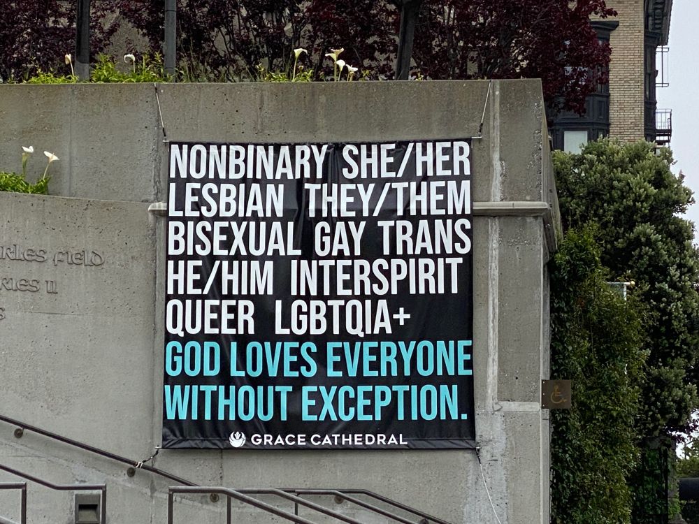 A poster on the wall of Grace Cathedral in San Francisco taken in 2023. The text on the poster says: Nonbinary, she/her, lesbian, they/them, bisexual, gay, trans, he/him, interspirit, queer, LGBTQIA+. God loves everyone without exception.