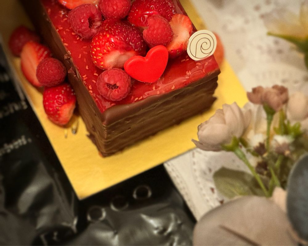 たっぷりのベリーソースにたくさんの苺とラズベリーがのったチョコレートムースの四角いホールケーキ