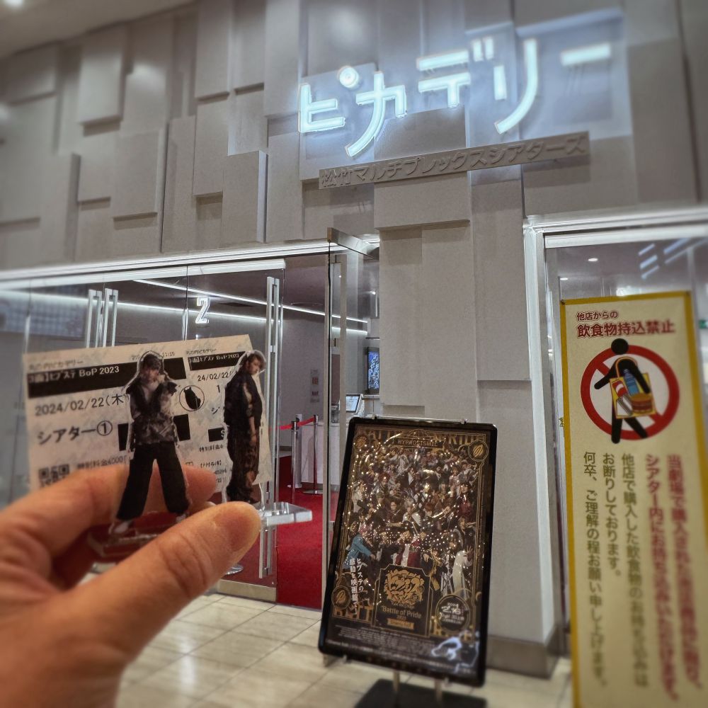 映画館入口で映画のポスターと推しのアクリルスタンドの記念撮影