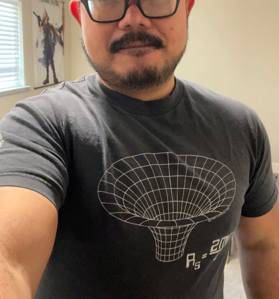 Guy wearing a black shirt with a graphical representation of a black hole, and a partially obscured equation for calculating the Schwarzchild radius.