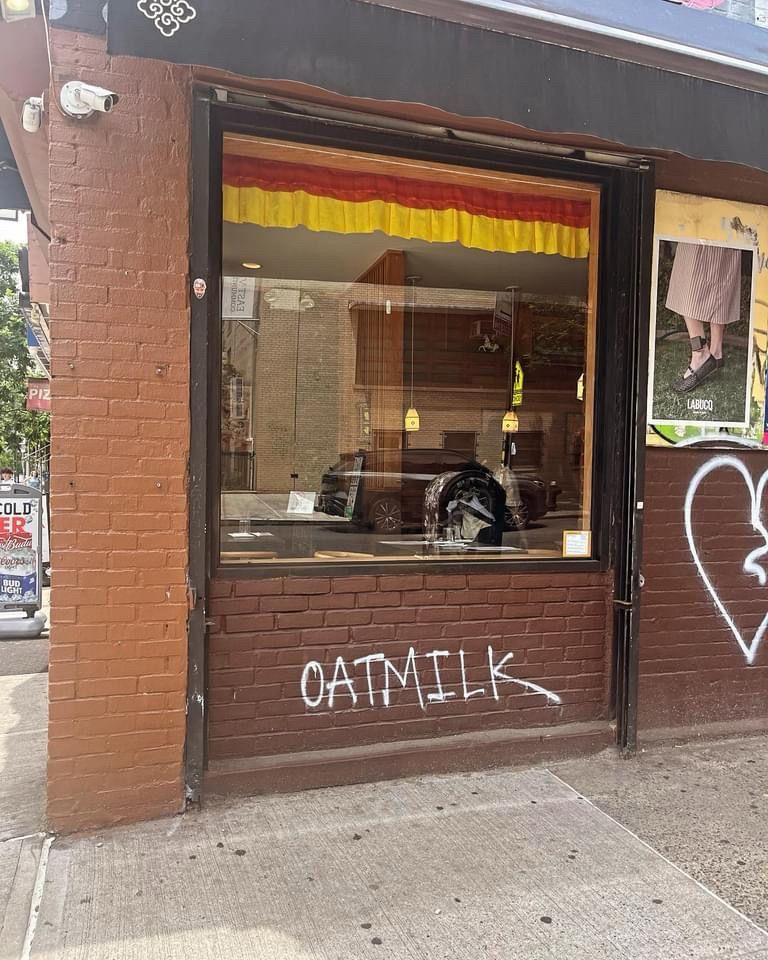 Exterior of a restaurant, where someone has written the word “oatmilk” in white spray paint