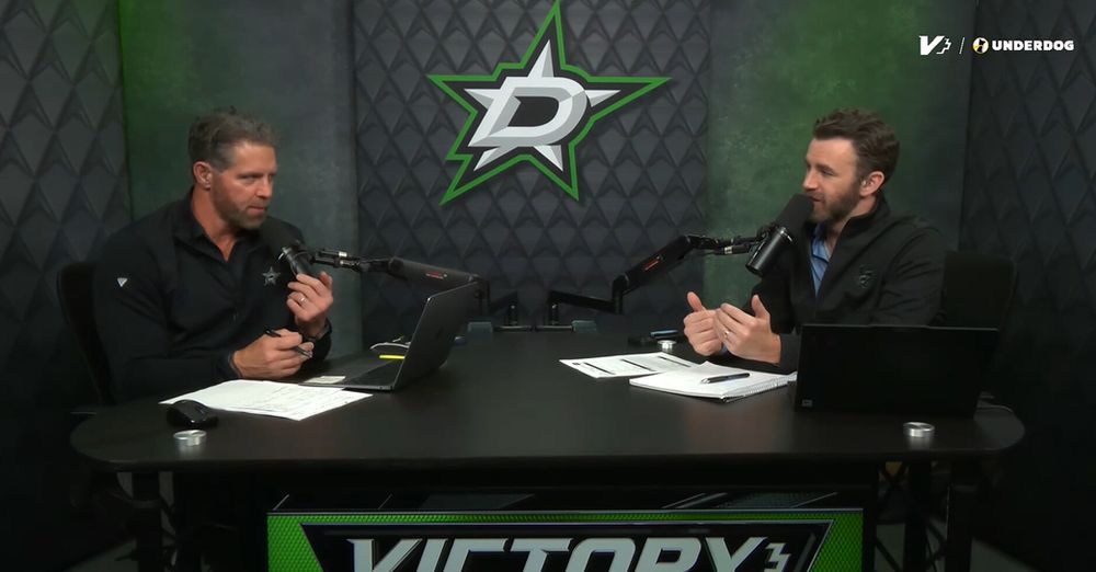 Two bearded white guys sit at a small black desk with small laptops and huge microphones in front of them. Right behind them is a cheap-looking back drop with the Dallas Stars logo on it.