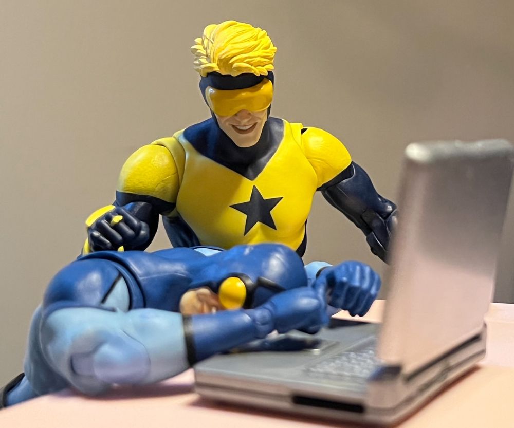 Booster gold action figure puts his hand on sleeping ted Kord action figure