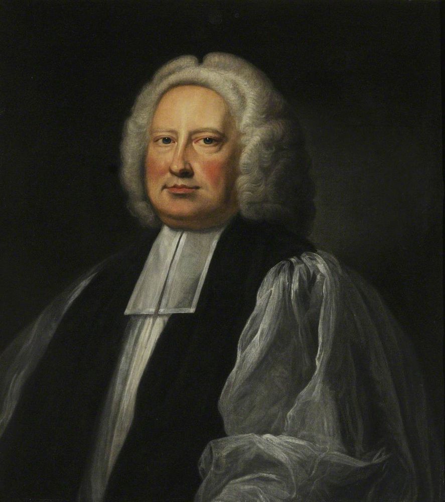 Portrait of a ruddy-faced middle-aged man in 18th-century clerical dress. He wears a short grey wig, a white surplice with a black chimere over it and white preaching bands. 