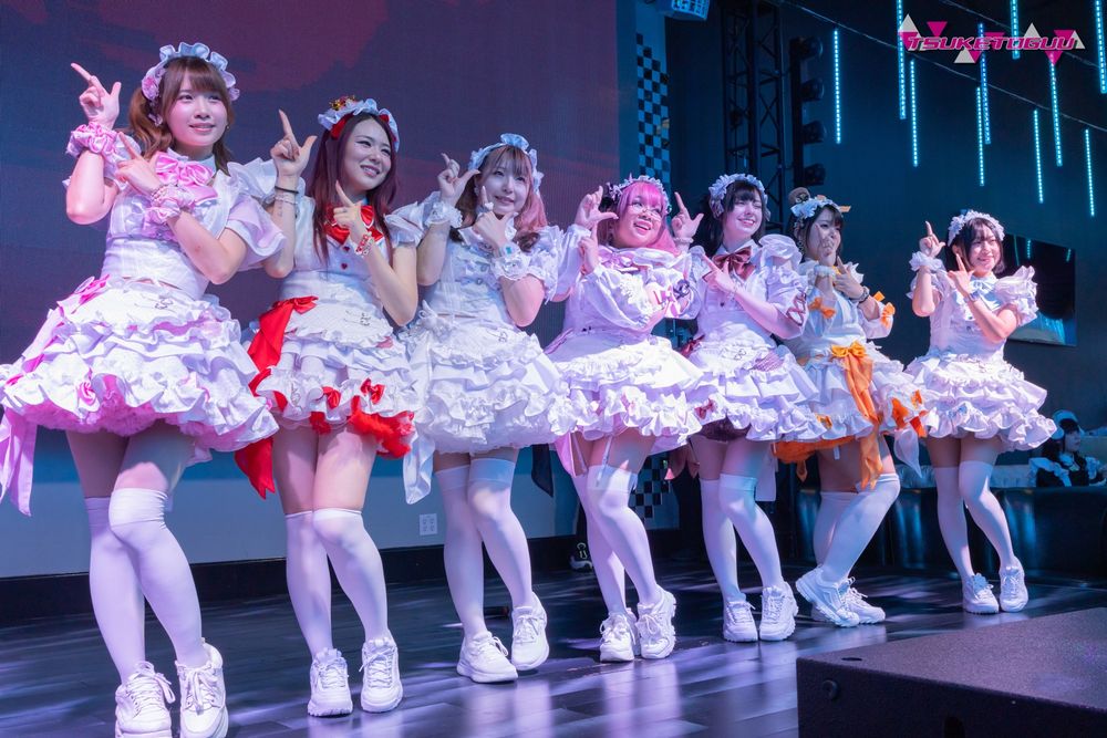 Photo of the seven-member idol maid group Moe↗Age!, posed in a line, hands pointed towards the upper-right.
