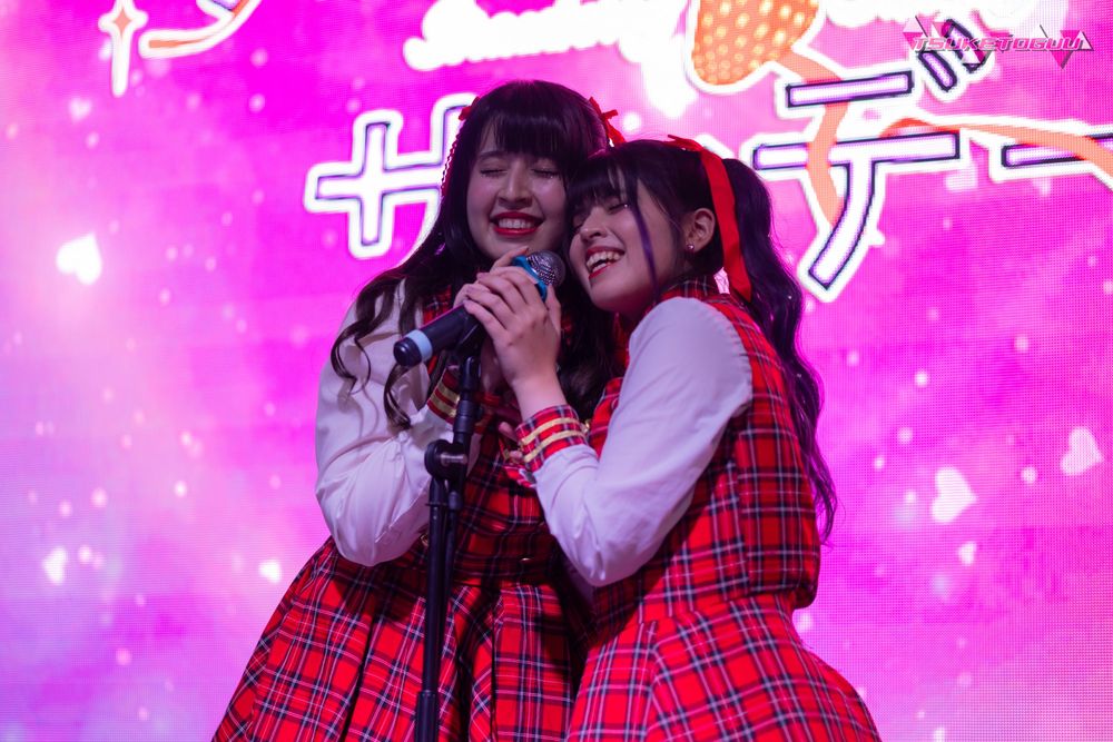 Photo of the duo group Strawberry Sunday, standing side by side in behind a stand microphone.