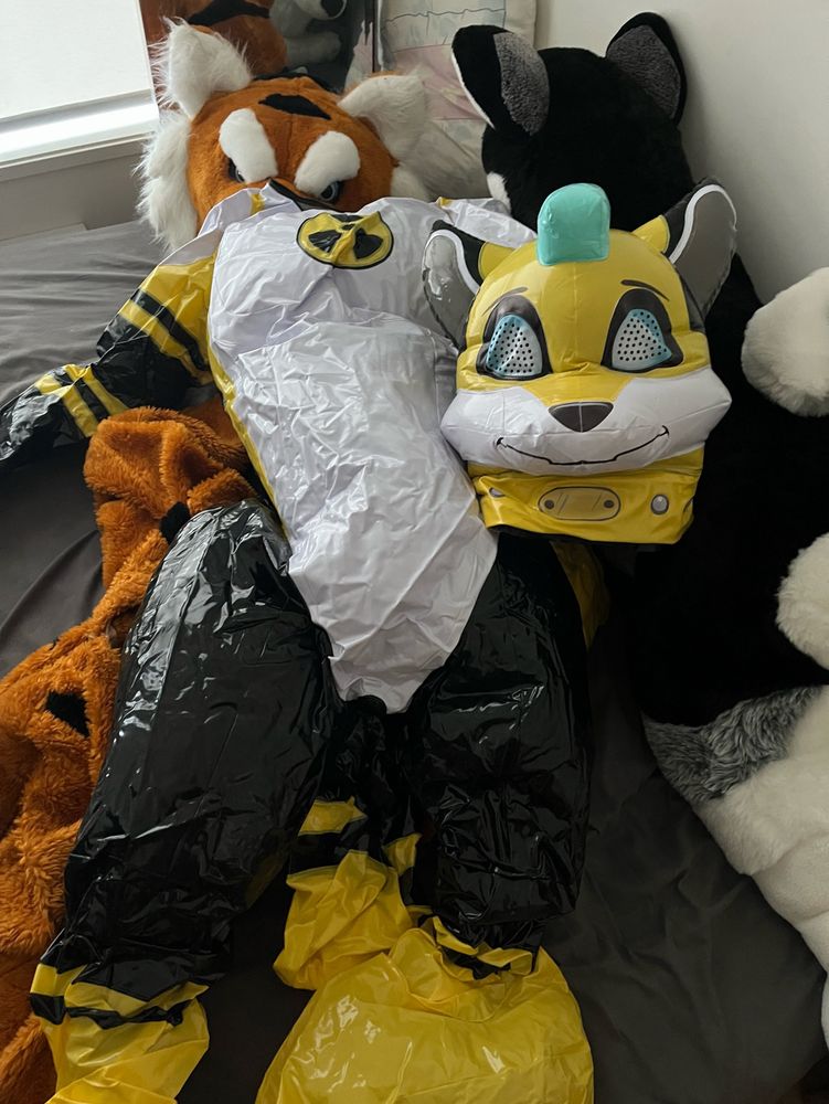 Partially inflated costume on a bed with a mascot suit and large plush. 