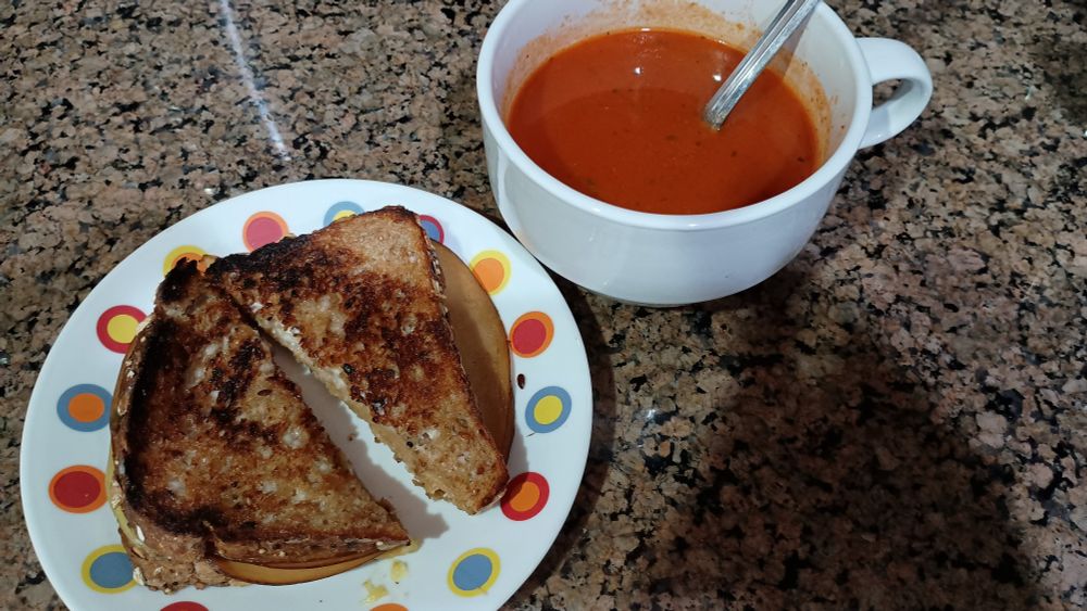 Grilled cheese sandwich on a small plate and a soup mug with tomato soup 