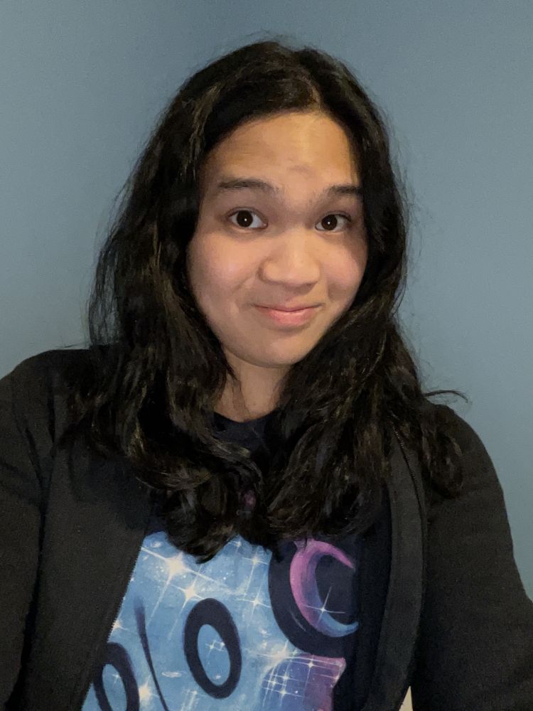 A photo of Hyla, taken August 2024. Hyla has wavy hair that reaches just below shoulder height. There's no facial hair and she looks significantly more confident in her appearance than she did four years ago.