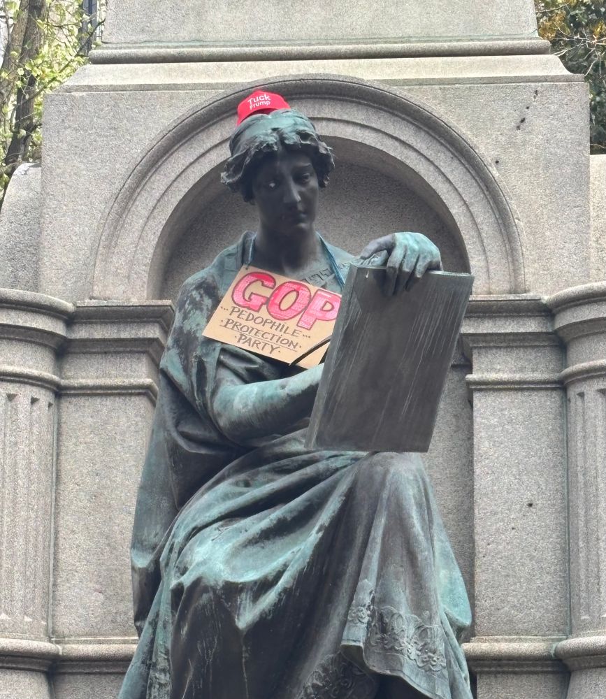 Monument adorned with what resembles a MAGA hat, but reads “tuck frump”.
Holding a sign that reads “GOP pedophile protection party”