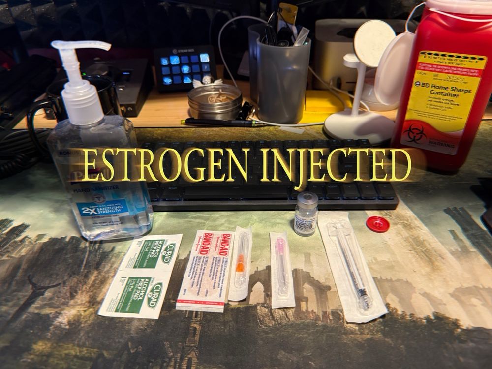 A desk with hormone injection supplies laid out: hand sanitizer, alcohol wipes, bandage, two gauges of needle, a vial of estrogen, a syringe, and a medical sharps container. The words “ESTROGEN INJECTED” are overlaid in the style of the text that appears when you defeat a boss in Dark Souls.
