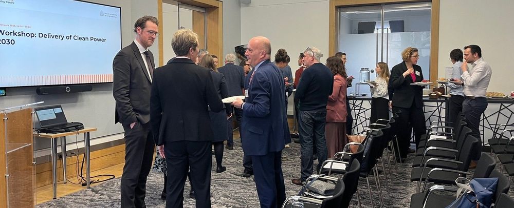 A group of people smartly dressed, networking and eating food in a room.