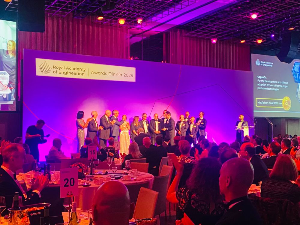 A group of people stand on a colourfully lit stage, while a room full of people seated at tables clap.