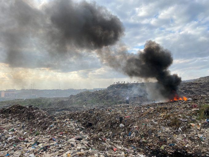 A fire burns among a wide expanse of openly dumped waste.