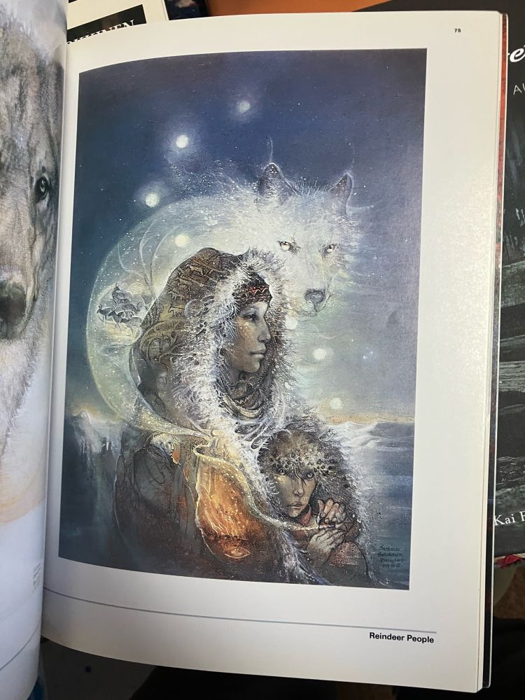 Photo of one of the pages of the book “Shaman the art of Susan Seddon Boulet” featuring the piece titled “Reindeer People”. In it there’s a blue and white snowy landscape, a woman and a child, and a white wolf in a dreamlike sky. Lots of small details like reindeer are depicted on top of the woman’s clothing.