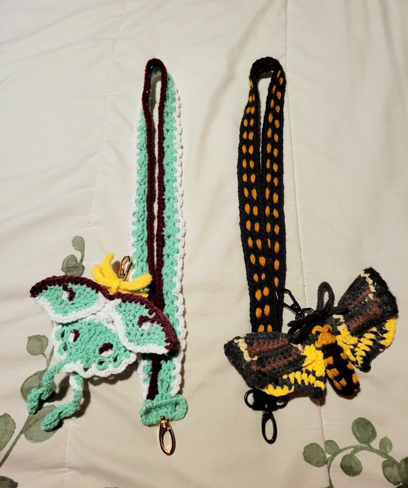 Left: green crocheted luna moth on a lanyard of the same colors
Right: black and yellow crocheted deaths head hawkmoth on a similarly colored lanyard