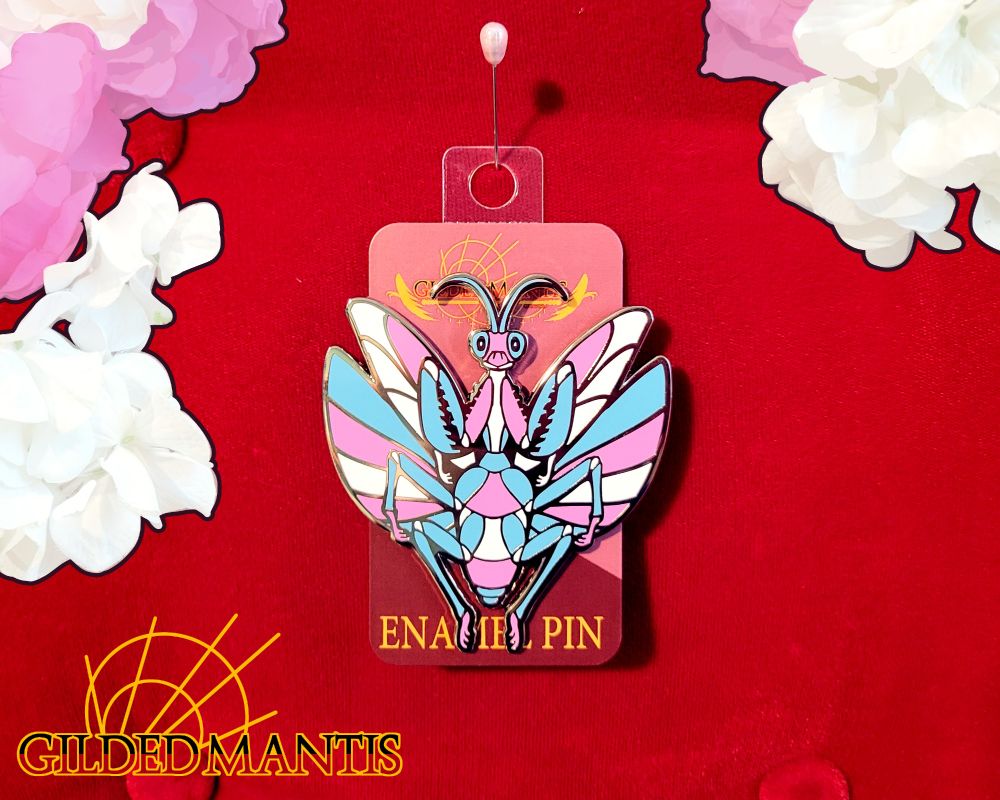 A 3 inch silver enamel pin of a praying mantis with open wings. It features colors from the Transgender pride flag