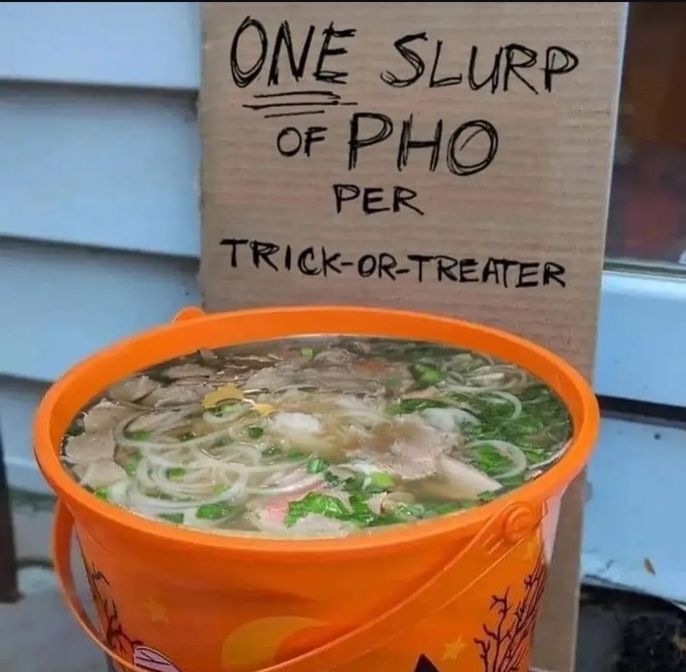 A Halloween bucket of pho soup with a cardboard sign behind that reads "one slurp of pho per truck-or-treater"
