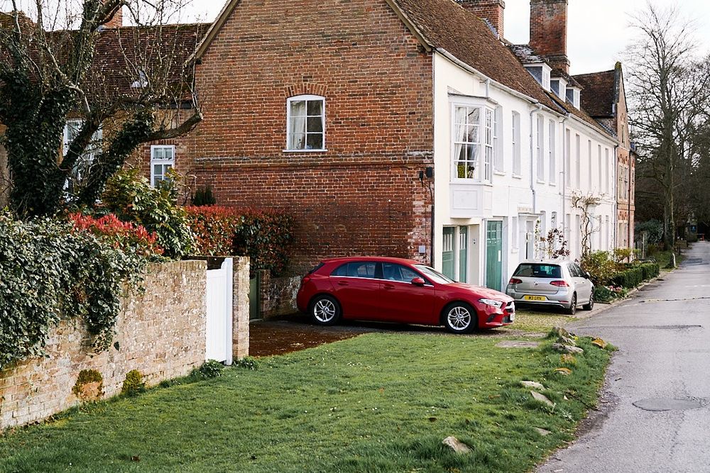 Old mews houses, painted white/cream with dark green doors. Red Mercedes car parked on the left of one house, and silver VW parked at the front of another house. 