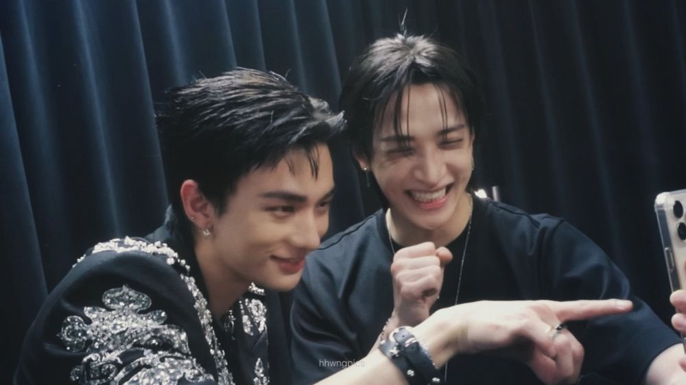 screenshot of the recent skz talker go episode 27! left is hyunjin and right is chan. both are wearing black outfits and both have black hair. they're smiling at a phone chan is holding in front of them.