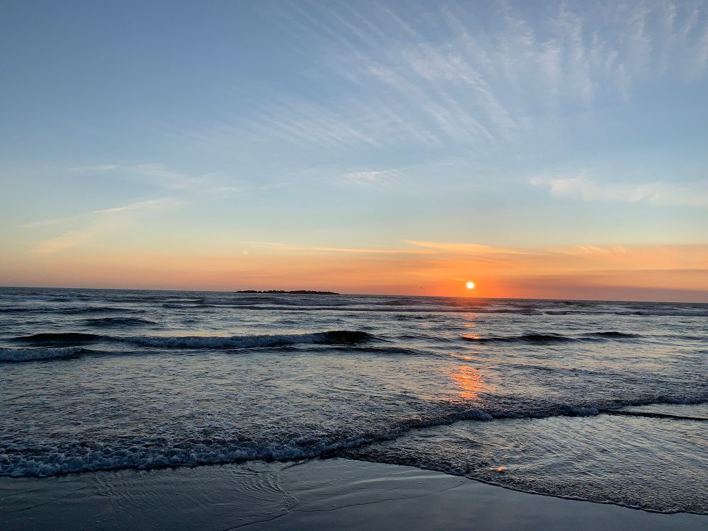 The sun is setting in an orange glow, over a dark-gray ocean. This was taken at a beach in Oregon in 2021.