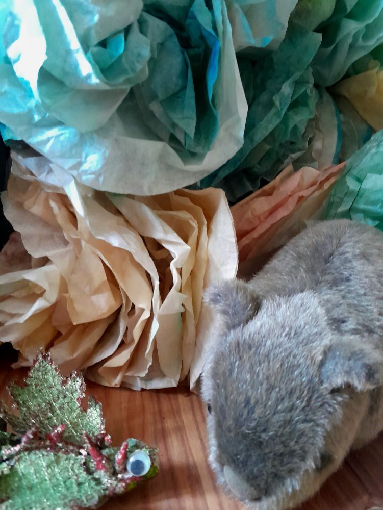 A small glittery dragon is talking to a cuddly wombat in front of pastel flowers made from the big flower-shaped coffee filters dyed with natural dyes, & the water left over after painting