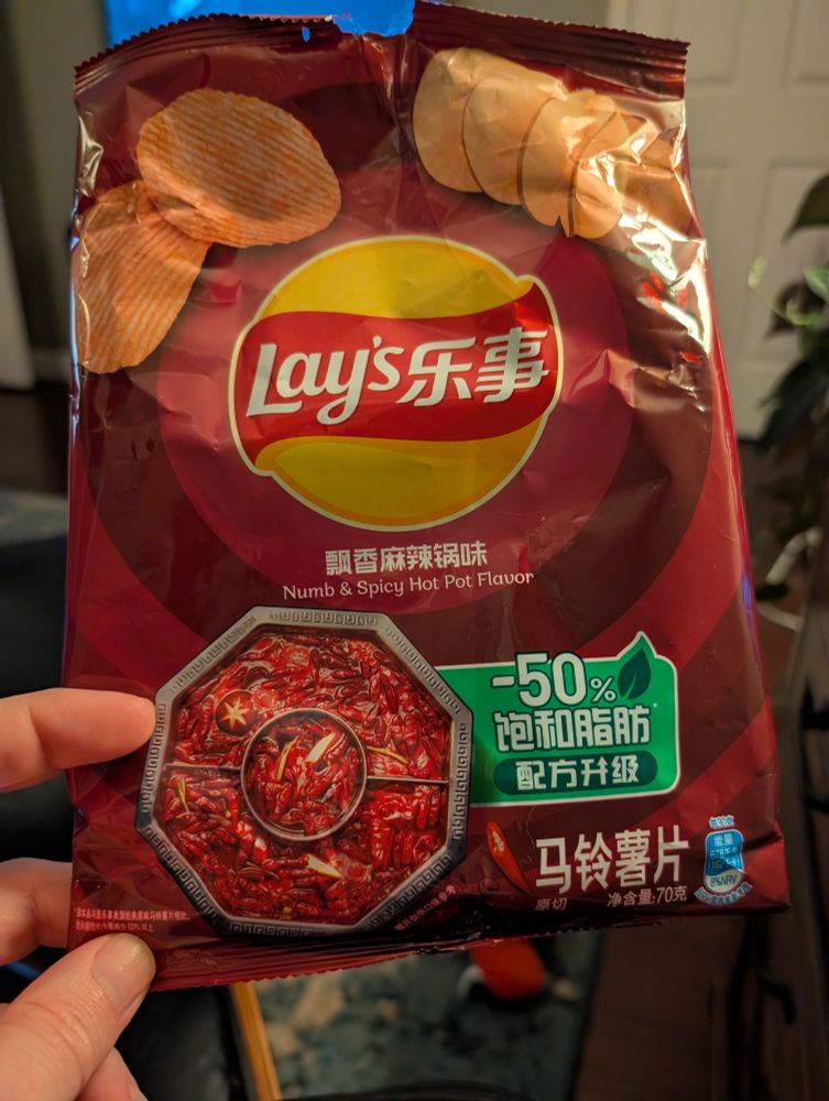 Empty bag of chips where all the writing is Chinese. Pink bad with a Lays logo, and a Chinese hotpot on it. 