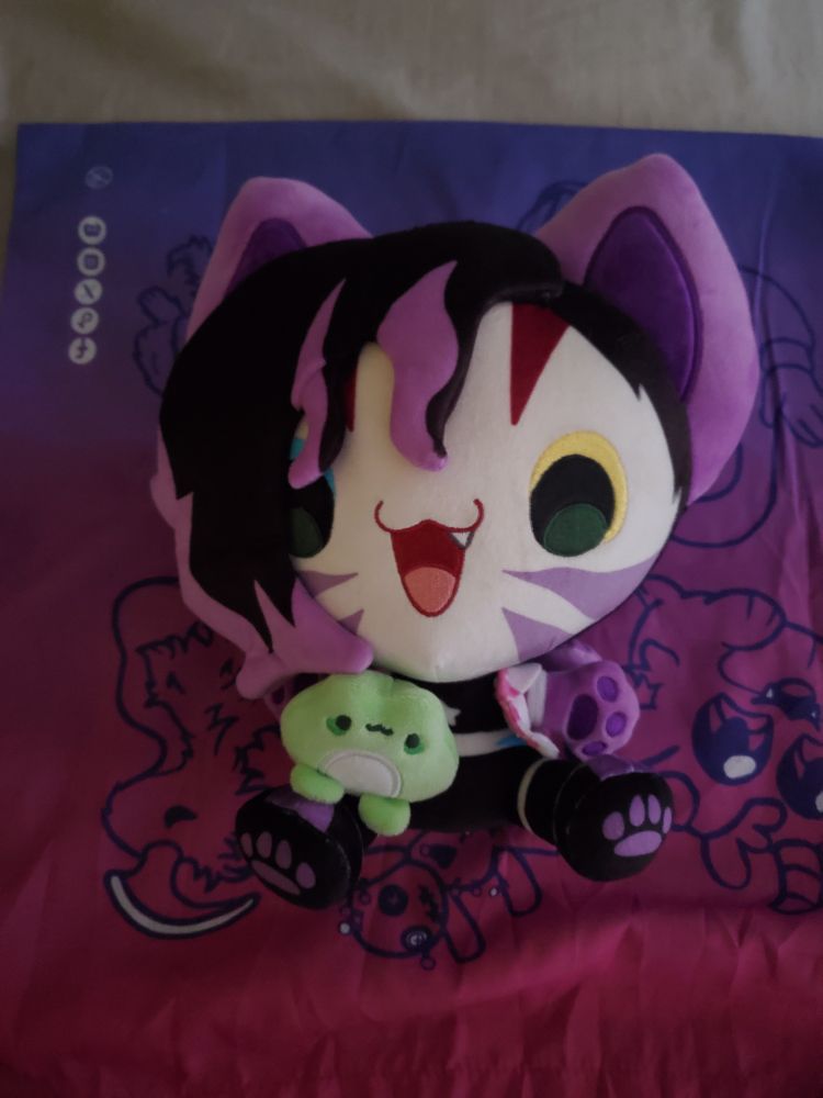 Medium sized cartoony plush doll of a purple and black cat girl with tiger stripes holding a frog. It's a plush of the twitch streamer Megaa for those who know.