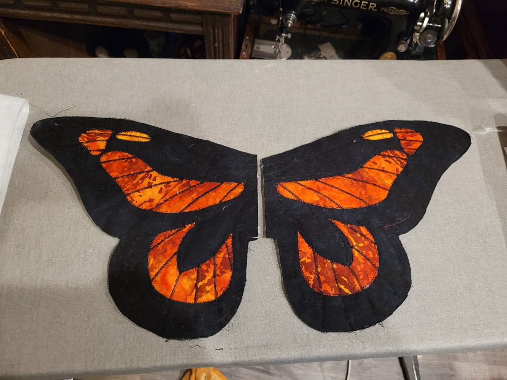 Half finished quilted monarch butterfly wings on an ironing board. 