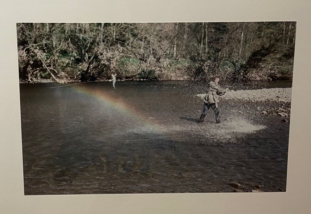 Photograph, one of a series in which the artist thrashes a river with a big stick, creating a rain arcing away from him. 