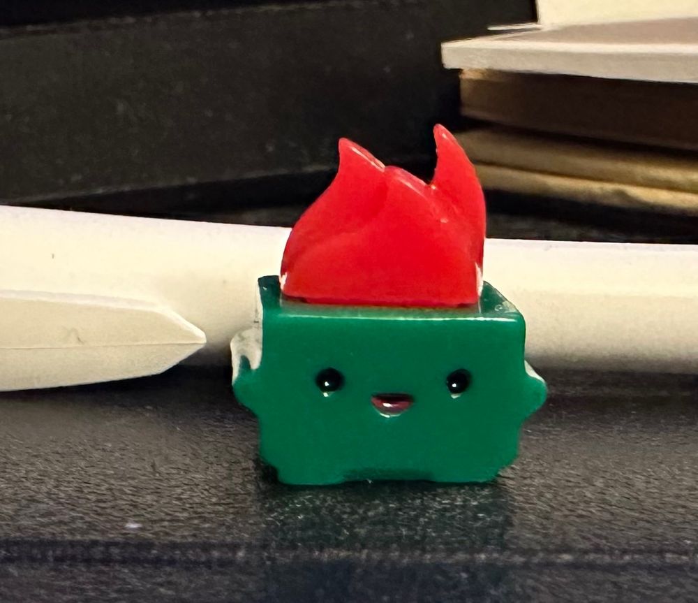 a tiny dumpster fire toy with a little face that appears to be enjoying its fate