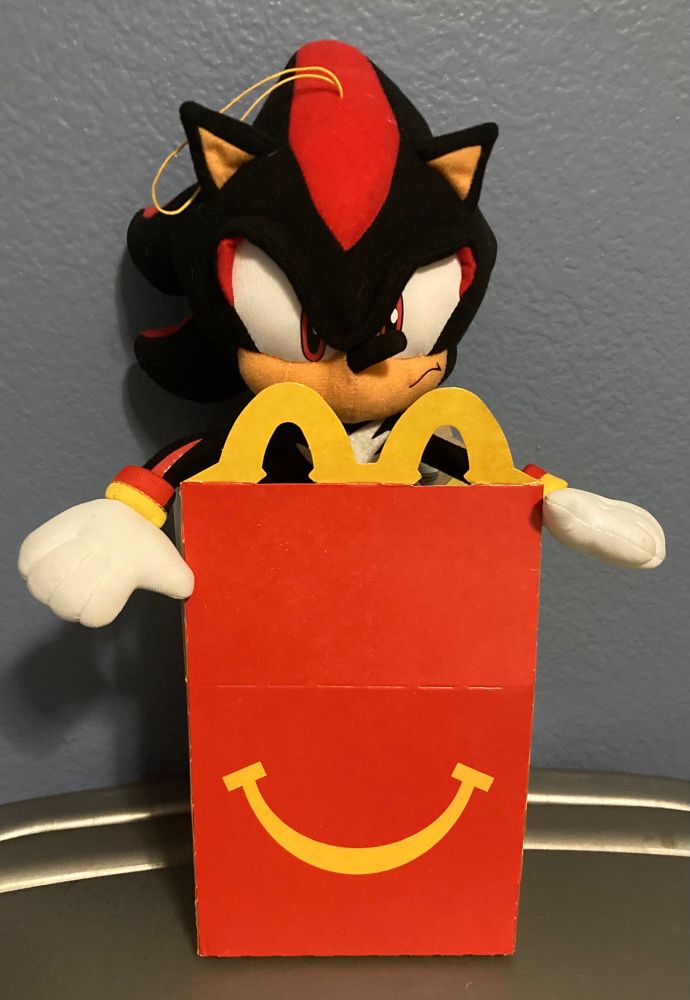 a photo of a shadow the hedgehog plush placed inside a mcdonald’s happy meal box