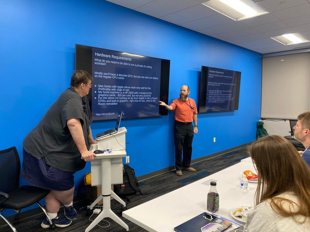 Two presenters at a user group in front of an audience, showcasing a slide on Hardware Requirements for running a Private AI coding assistant
