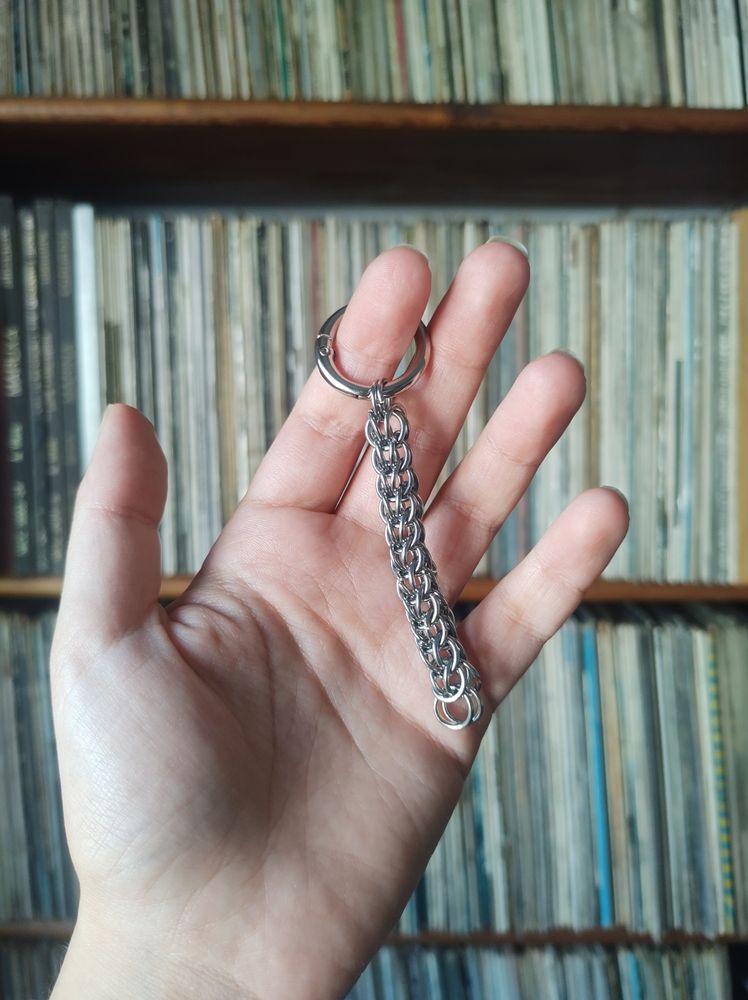 Fragmento de una cadena hecha con arandelas de acero inoxidable con el patrón full persian 6 en 1, mi mano está en mi primer plano sujetando la cadena, de fondo hay una estantería con vinilos difuminada 