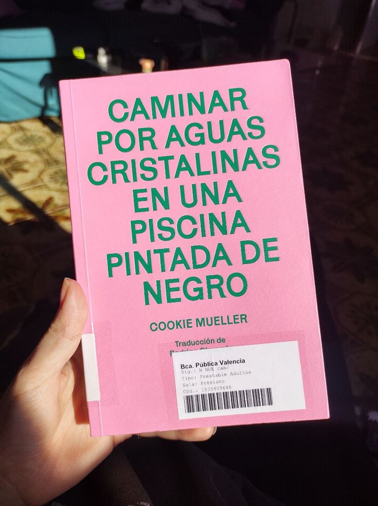 Foto de la portada del libro "Caminar por aguas cristalinas en una piscina pintada de negro", escrito por Cookie Mueller, traducido por Rodrigo Olavarría y editado por Los Tres Editores. Este ejemplar tiene una pegatina en la portada que indica que es de la Biblioteca Pública de Valencia.