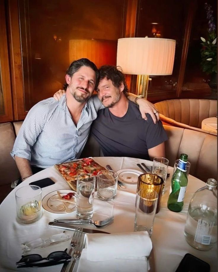 Fofo de Pedro Pascal e Franklin Latt sentados em um restaurante. Eles estão com os rostos próximos e as mãos no ombro um do outro.