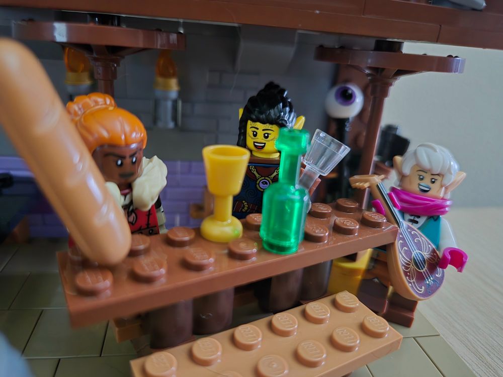 Zoom in photo of the grand time around the table. The Bard with her Lute, singing her tales. The Rogue chatting with infectious energy, fresh off an empty glass. And the Barbarian, wielding a full baguette and a determined look in her eye.