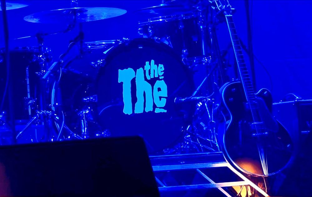 Drumstel van The The op een blauwverlicht podium.