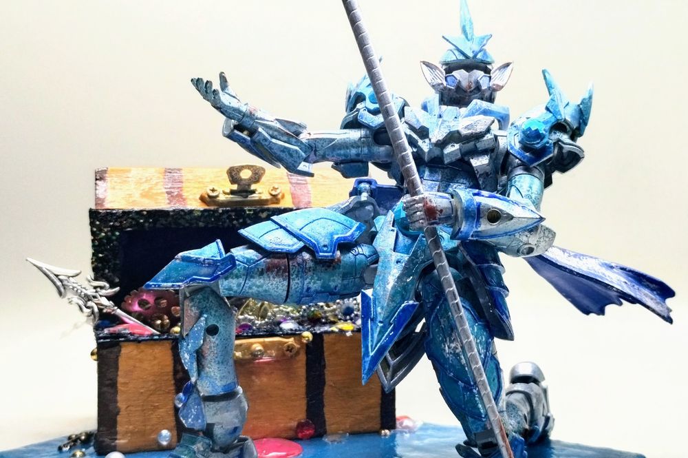 A knight Gundam that looks water worn. Behind it is an overflowing treasure chest. 